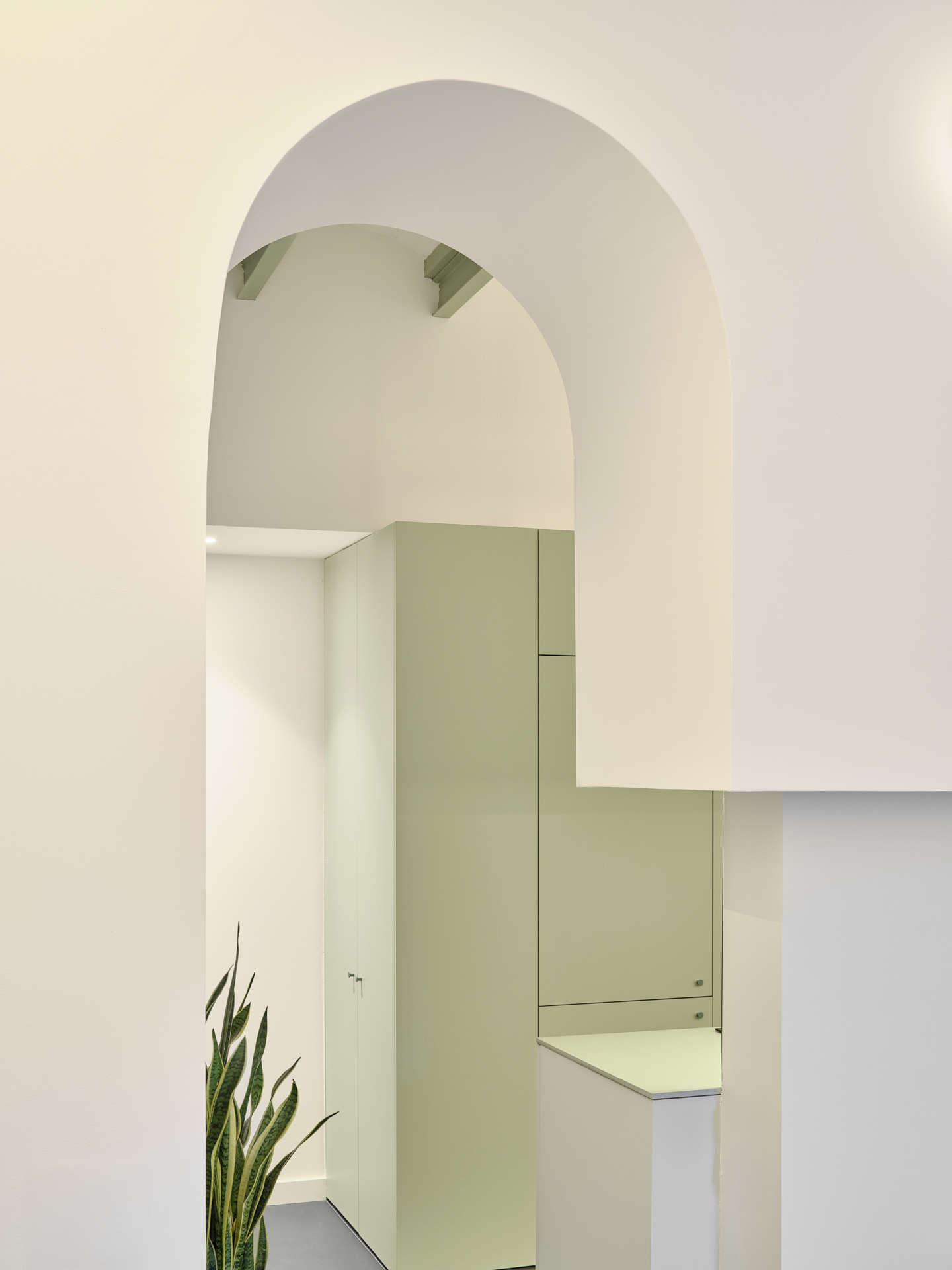 Arched opening framing the soft green kitchen volume in CRÜ’s “La Dolors” renovation, beneath the restored ceramic structure.